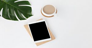 Image of an iPad on a notebook on a desk. On the upper right of the iPad there is a white cup of hot chocolate sitting on a coaster. On the upper left of the the iPad there is a green palm leaf: This article is about content marketing